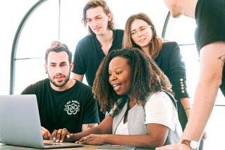 A diverse group of young professionals collaborating around a laptop in a modern office setting. Perfect for business or tech concepts.